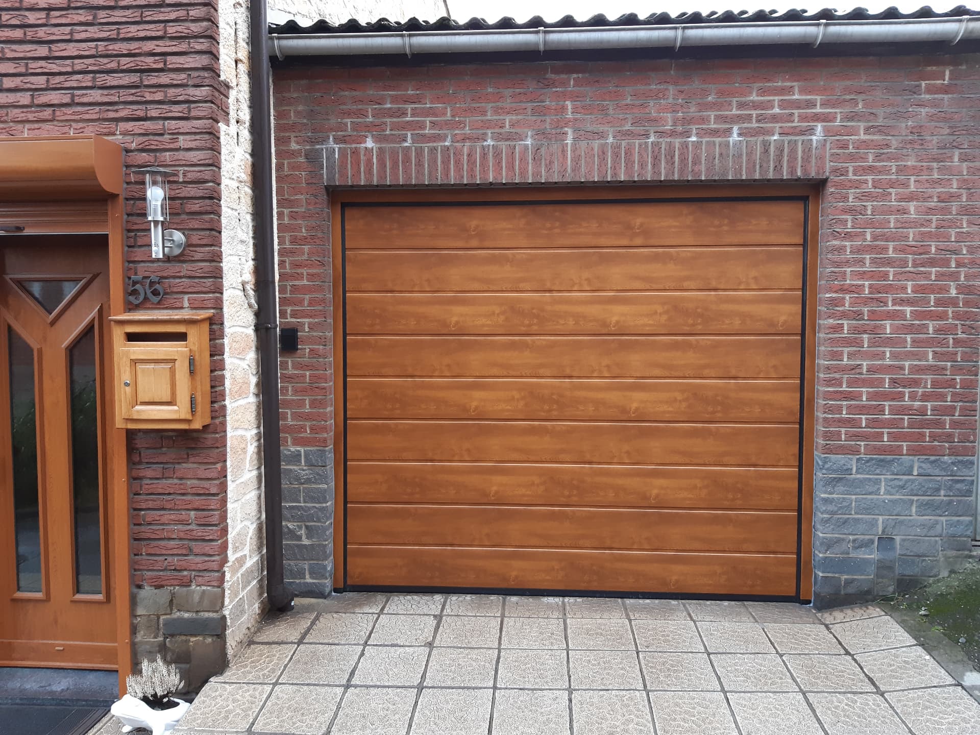 Porte de garage sectionnelle décor chêne doré sur façade en briques