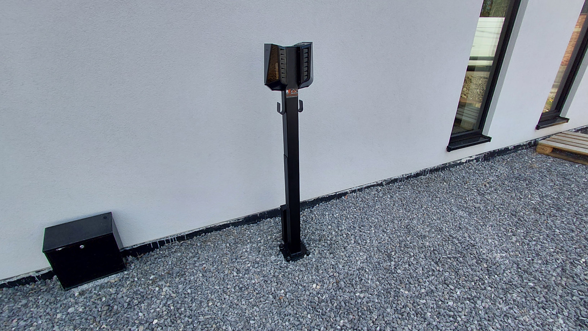 Borne de recharge noire sur pied installée le long d'une façade