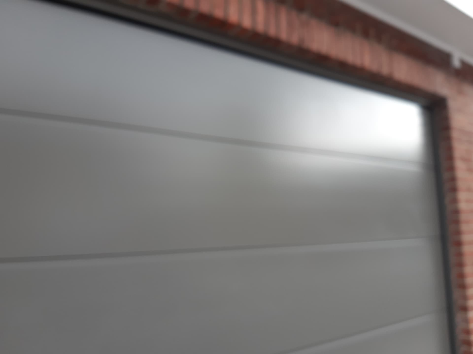 Porte de garage sectionnelle gris clair posée sur façade en briques